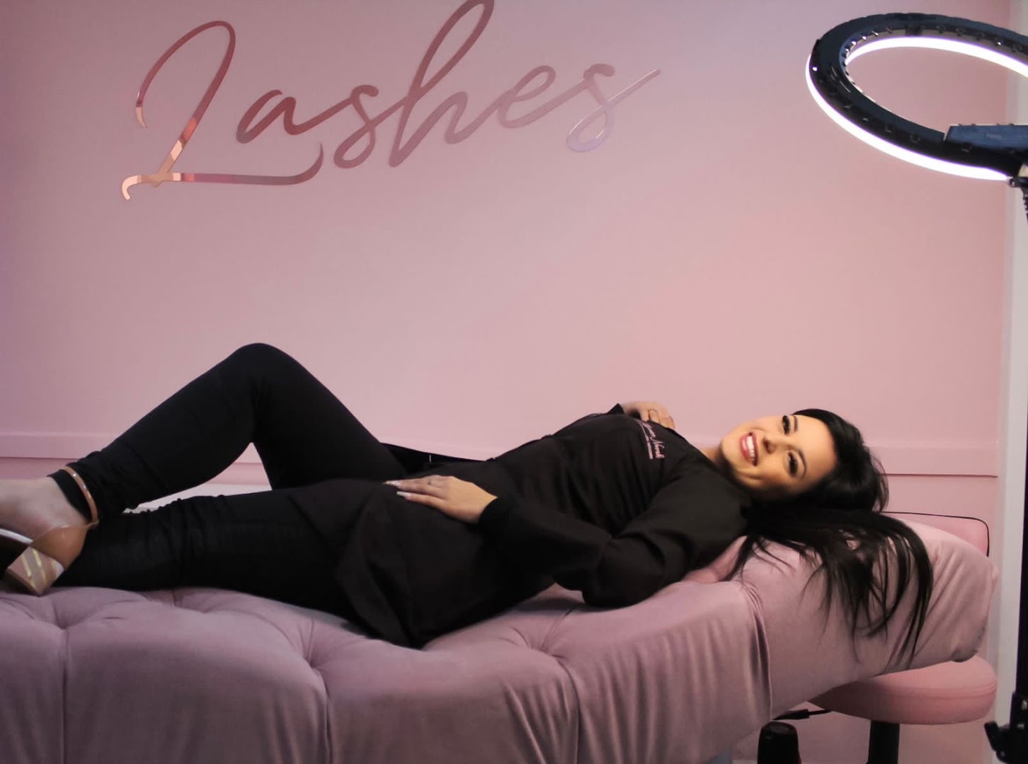 Interior rosa do Studio Thaynara Novak, com maca de atendimento, ring light e a palavra Lashes pintada na parede